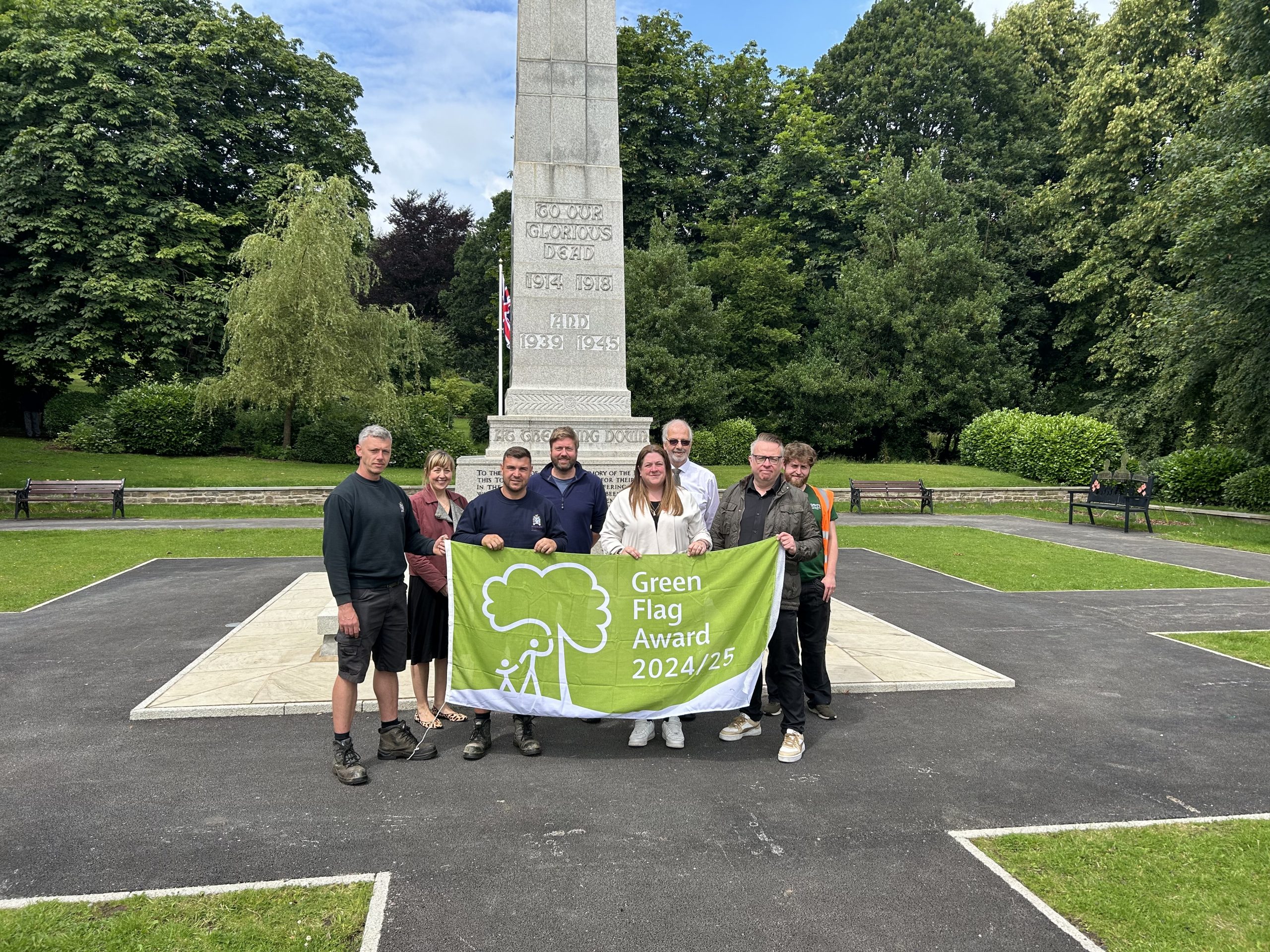 Several people holding Green Flag in front of the war memorial at Memorial Park, Great Harwood